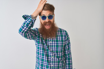 Young redhead irish man wearing casual shirt and sunglasses over isolated white background surprised with hand on head for mistake, remember error. Forgot, bad memory concept.