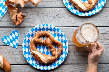 Oktoberfest traditional food and beer. Hand holding beer mug, pretzels on paper plates