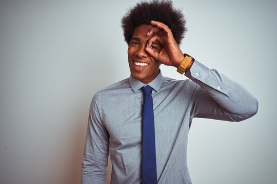 American business man with afro hair wearing shirt and tie over isolated white background doing ok gesture with hand smiling, eye looking through fingers with happy face.