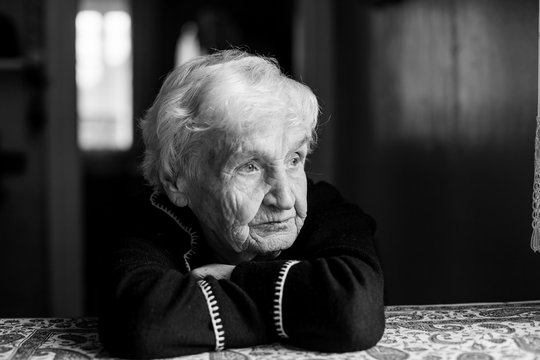 Portrait of lonely old woman sits at the table. Black and white photo.