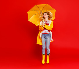 young happy emotional cheerful girl laughing and jumping with yellow umbrella   on colored red background.