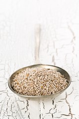 White whole, organic chia seeds heap in silver metal spoon on white rustic table background with selective focus