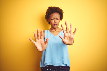 Beautiful african american woman wearing elegant shirt over isolated yellow background afraid and terrified with fear expression stop gesture with hands, shouting in shock. Panic concept.