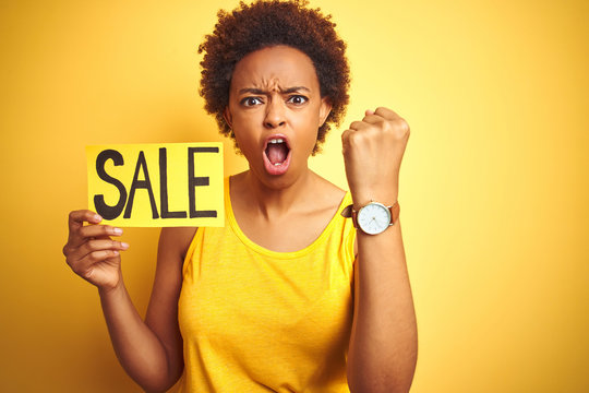 African american woman holding sale board over yellow isolated background annoyed and frustrated shouting with anger, crazy and yelling with raised hand, anger concept