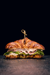 Croissant sandwich with fresh salad, ham and cream cheese on dark background