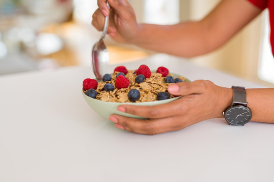Close up of young woman eating healthy cereals and berries for breakfast