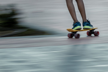 Blurred anonymous teenager riding skateboard on pavement of town street