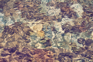 Abstract pattern of pebbles under the surface of the water, texture. Rock bottom background seen through clear water in mountain lake