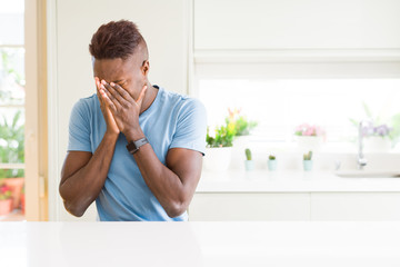 Handsome african american man wearing casual t-shirt at home with sad expression covering face with...