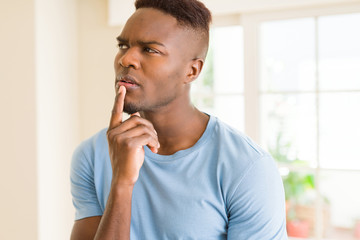 Handsome young african man thinking and questioning with pensive face, hand on chin wondering about...