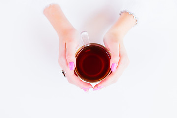 The girl holds a warm cup of tea with two hands on a white table