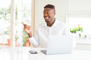African american business man working using laptop with a big smile on face, pointing with hand and finger to the side looking at the camera.