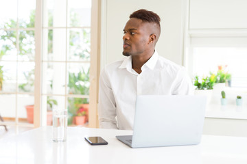 African american business man working using laptop looking to side, relax profile pose with natural face with confident smile.