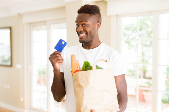 African american man holding paper bag full of groceries and holding credit card as payment