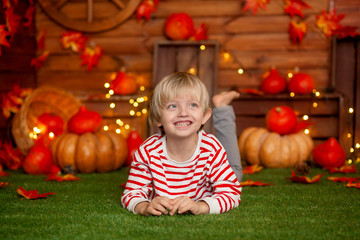 Fototapeta na wymiar Happy cute boy 5-6 years old in a striped sweater on a green rug in the autumn decor with pumpkins, holiday Halloween