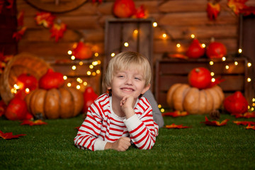 Fototapeta na wymiar Happy cute boy 5-6 years old in a striped sweater on a green rug in the autumn decor with pumpkins, holiday Halloween