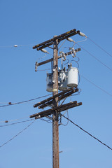 Low angle upward view of a tall electricity distribution pole with power lines seen against a clear blue sky