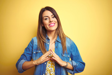 Young beautiful woman standing over yellow isolated background Hands together and fingers crossed smiling relaxed and cheerful. Success and optimistic