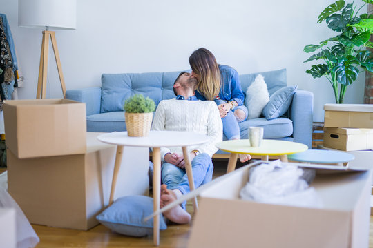 Young beautiful couple sitting on the sofa drinking cup of coffee at new home around cardboard boxes