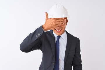 Young handsome architect man wearing suit and helmet over isolated white background smiling and laughing with hand on face covering eyes for surprise. Blind concept.