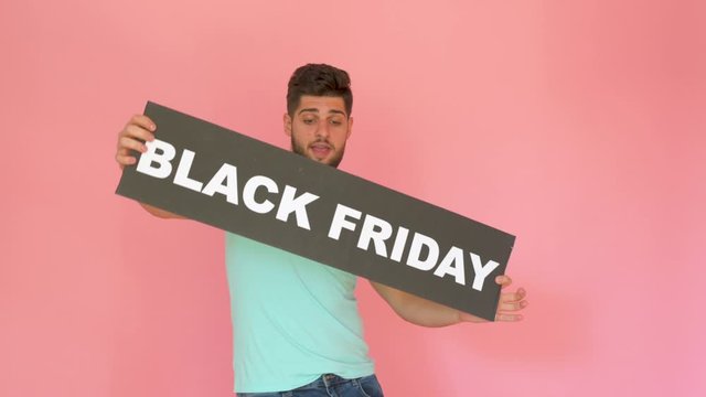 handsome funny smiling guy with black friday sign dancing isolated over pink