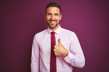 Young business man wearing elegant shirt and tie over purple isolated background doing happy thumbs up gesture with hand. Approving expression looking at the camera with showing success.