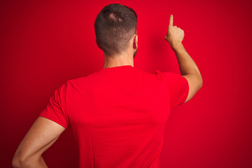 Young handsome man wearing casual t-shirt over red isolated background Posing backwards pointing...