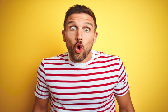 Young handsome man wearing casual red striped t-shirt over yellow isolated background afraid and shocked with surprise expression, fear and excited face.