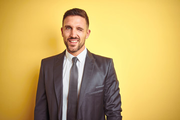Young handsome business man over yellow isolated background winking looking at the camera with sexy...