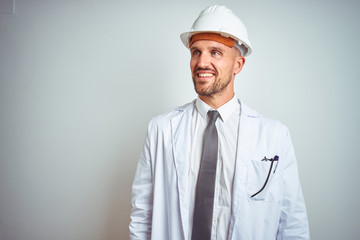 Young handsome engineer man wearing safety helmet over isolated background looking away to side with smile on face, natural expression. Laughing confident.