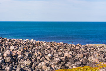 Large round cut stones seascape diagonally. The deep azure color of a calm ocean. Rocky beach on the Barents sea near Teriberka, Murmansk region