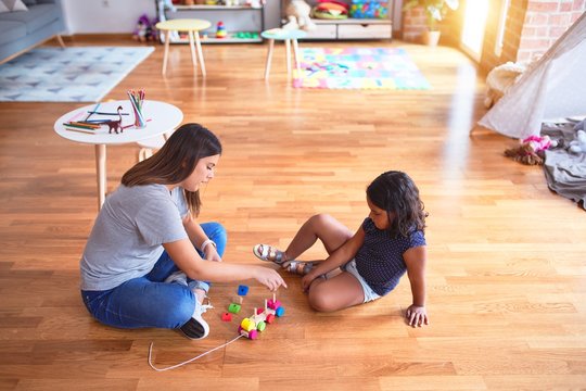 Beautiful teacher and toddler girl playing with train at kindergarten