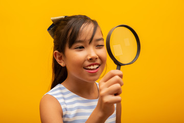 Portrait of happy little Asian child with magnifying glass.