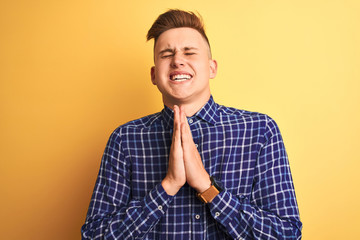 Young handsome man wearing casual shirt standing over isolated yellow background begging and praying with hands together with hope expression on face very emotional and worried. Asking for forgiveness