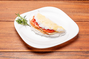 Tapioca filled with ham, cheese and tomato, on wooden background. Flatbread made from cassava (also known as casabe, bammy, beiju, bob, biju).