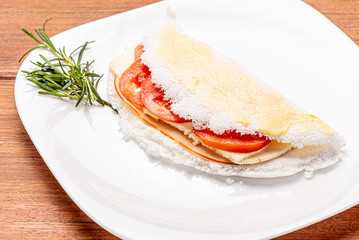Tapioca filled with ham, cheese and tomato, on wooden background. Flatbread made from cassava (also known as casabe, bammy, beiju, bob, biju).