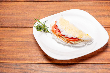 Tapioca filled with ham, cheese and tomato, on wooden background. Flatbread made from cassava (also known as casabe, bammy, beiju, bob, biju).