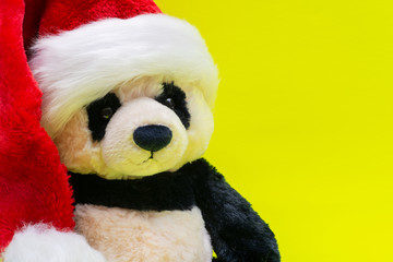 Panda Bear stuffed plush toy wearing Red White Christmas Plush Santa Hat on bright yellow background. Christmas, New Year, Winter Holidays concept.