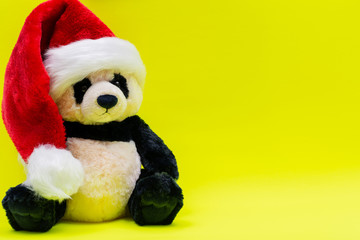 Panda Bear stuffed plush toy wearing Red White Christmas Plush Santa Hat on bright yellow background. Christmas, New Year, Winter Holidays concept.
