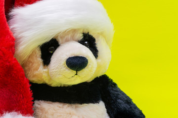 Panda Bear stuffed plush toy wearing Red White Christmas Plush Santa Hat on bright yellow background. Christmas, New Year, Winter Holidays concept.