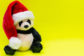 Panda Bear stuffed plush toy wearing Red White Christmas Plush Santa Hat on bright yellow background. Christmas, New Year, Winter Holidays concept.