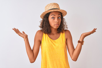 Young brazilian woman wearing yellow t-shirt and summer hat over isolated white background clueless...