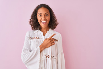 Young brazilian woman wearing shirt standing over isolated pink background cheerful with a smile of face pointing with hand and finger up to the side with happy and natural expression on face