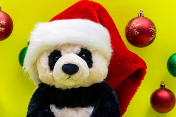 Panda Bear plush toy with Red Christmas Santa Hat surrounded by Colorful Vintage Ornaments on bright yellow background. Winter Holidays concept.