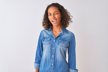 Young brazilian woman wearing denim shirt standing over isolated white background winking looking...