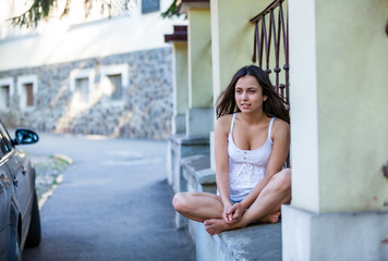 Outdoors portrait of beautiful young brunette girl sitting on street