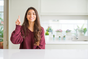 Young beautiful woman at home showing and pointing up with finger number one while smiling confident and happy.