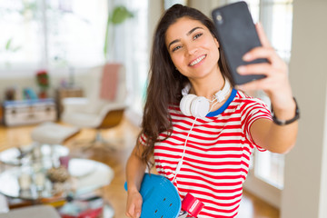 Beautiful skater woman smiling friendly standing with skateboard and taking a selfie using smartphone