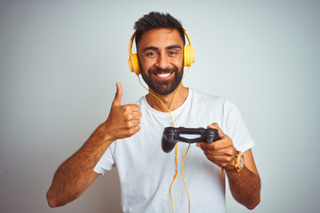 Arab indian gamer man playing video game using headphones over isolated white background happy with...