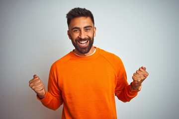 Young indian man wearing orange sweater over isolated white background celebrating surprised and...